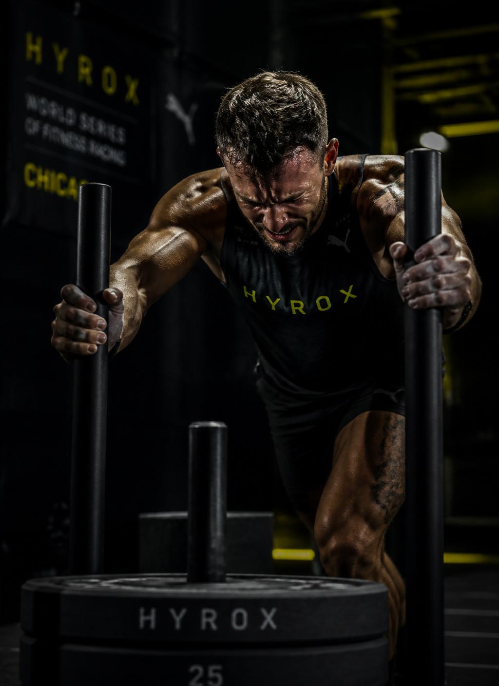 HYROX athlete pushing a heavy sled in a dark industrial gym